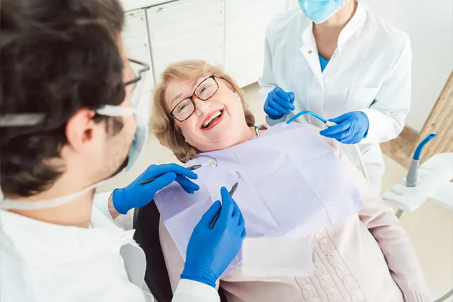 Dr. Italo Di Prisco and a dental assistant examining a smiling woman in dental chair.